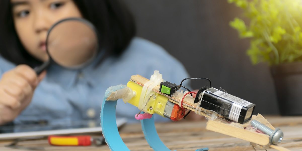 STEM Education concept. Study guide that integrates knowledge Science, Technology, Engineering, Math. Kids are holding a rocket paper, A student holding a magnifying glass watching the robot.